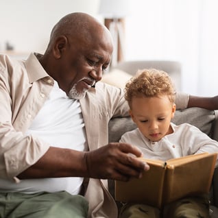 grandfather sitting on a couch with his grandson reading a book